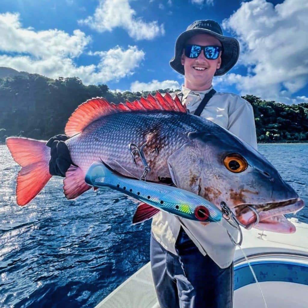 Angler holding a big reef red with a blue stickbait along Efate’s coastline in Vanuatu.