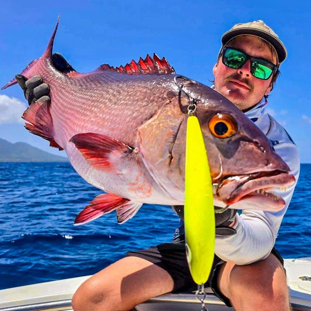 Angler presenting a large reef red with a bright yellow stickbait aboard a centre console in Vanuatu.