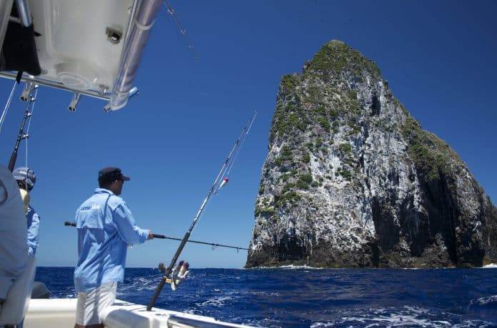 Anglers casting from a centre console beside a steep volcanic seamount in Vanuatu during spring–summer, targeting yellowfin, GTs and marlin.