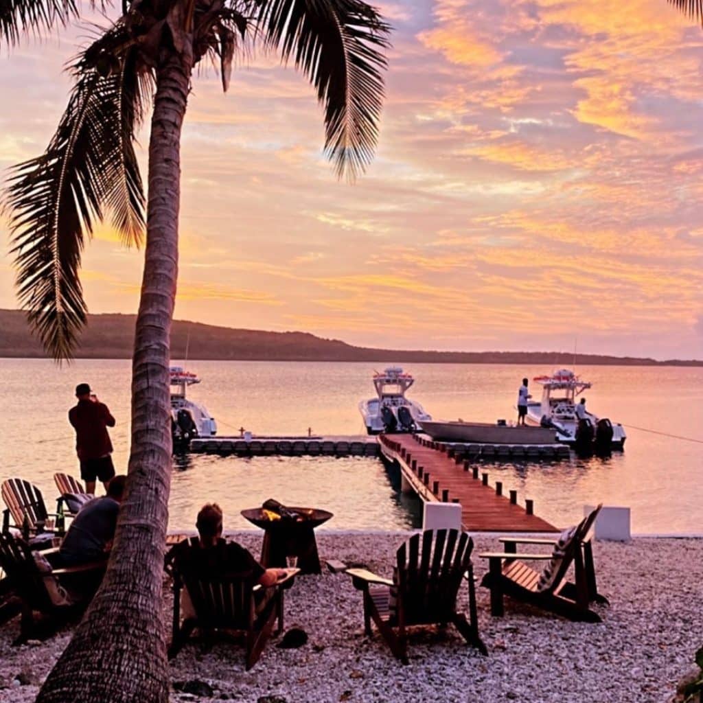 Fishing in Vanuatu September to December – Trees and Fishes Sunset Jetty | Ocean Blue Sunset at Trees and Fishes Private Retreat in Vanuatu with centre‑console boats at the jetty and guests relaxing by the firepit during the spring–summer fishing season.