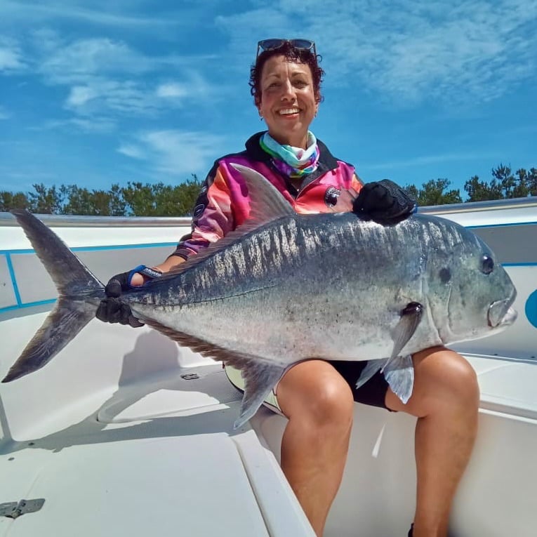 Angler on an Ocean Blue centre console holding a large GT with calm conditions near reef shoreline.