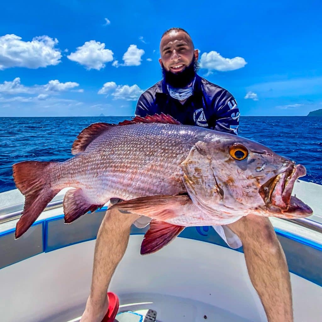 Angler holding a large reef red aboard an Ocean Blue centre console in bright blue conditions.