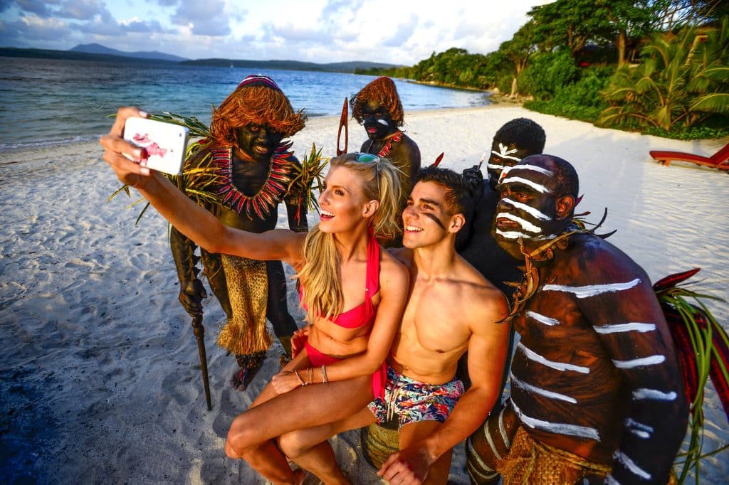 Guests taking a selfie with traditionally painted performers on a Vanuatu beach at sunset.