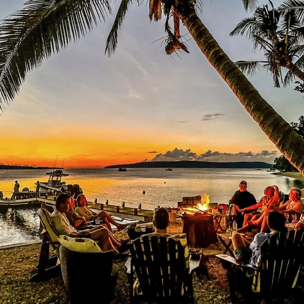 Guests relaxing at the Trees & Fishes firepit at sunset with boats moored on the private jetty.