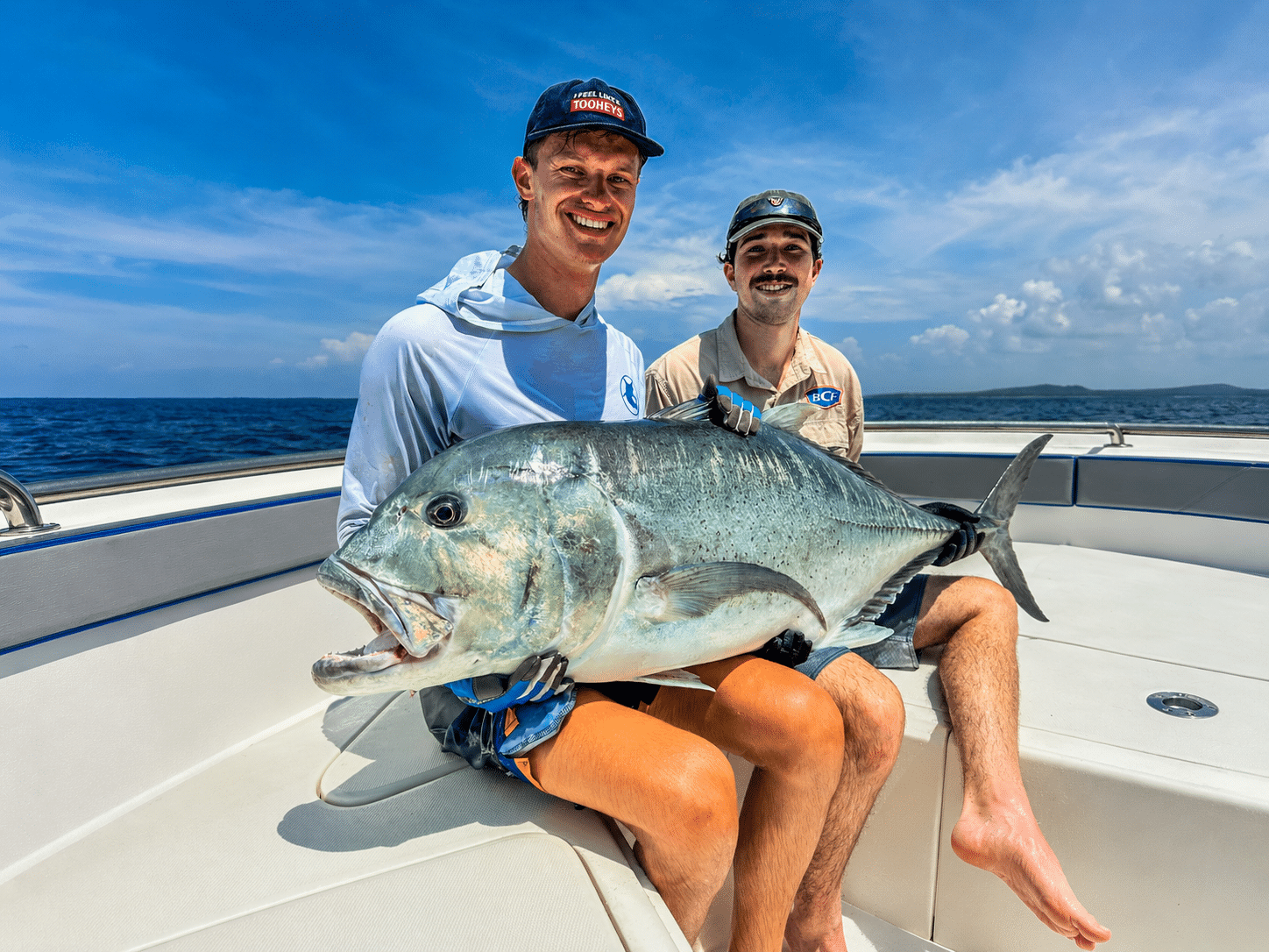 Angler holding a large Giant Trevally aboard a fishing boat in Vanuatu, showcasing a successful catch during a sport fishing adventure on tropical blue waters.