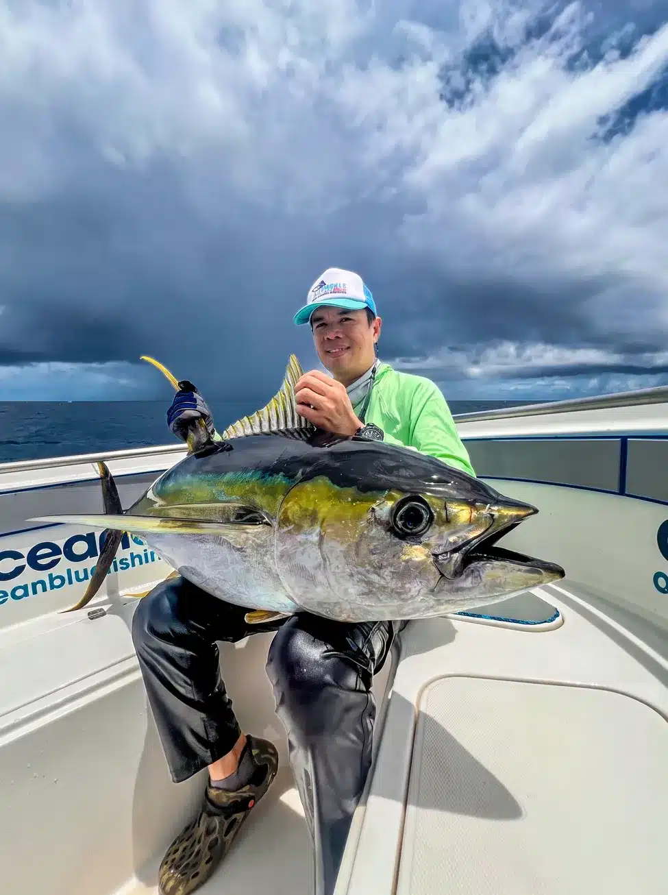 Angler holding a large yellowfin tuna on an Ocean Blue Fishing Adventures boat in Vanuatu, with dark storm clouds over the open ocean.
