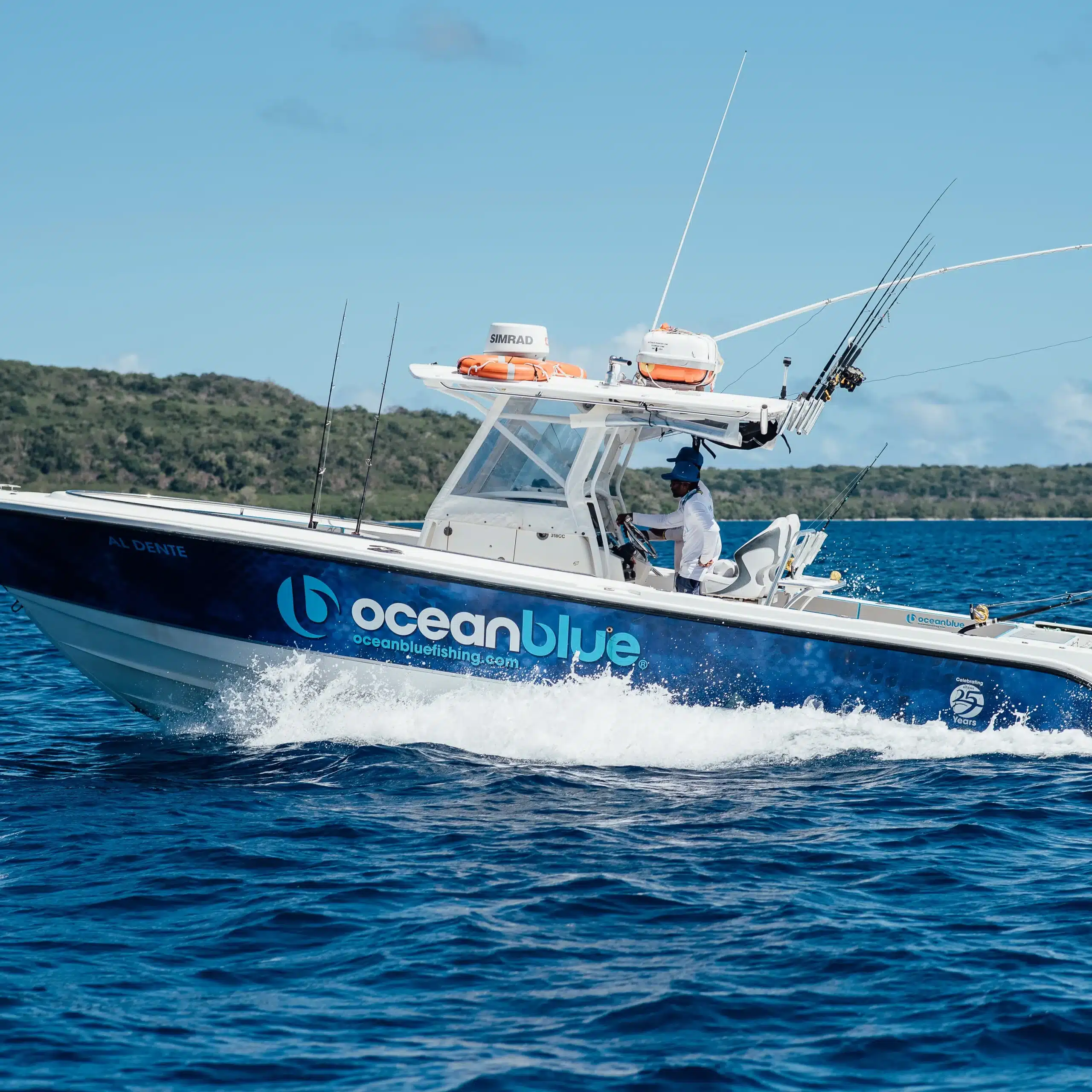 Ocean Blue Fishing Adventures sportfishing boat cruising on blue water in Vanuatu with multiple rods rigged, Ocean Blue branding on the hull and a tropical island coastline in the background.