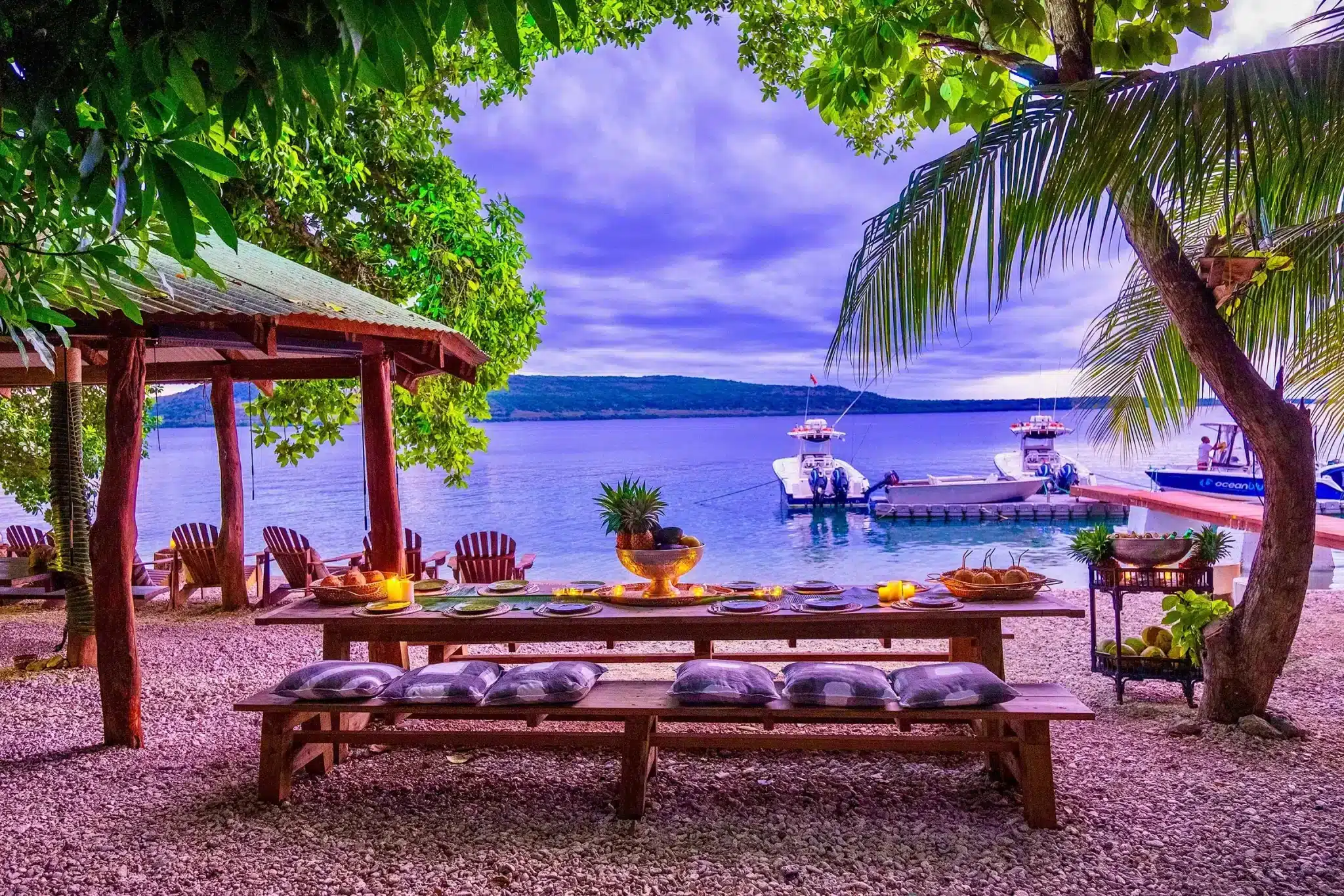 Beachfront outdoor dining area at Trees and Fishes Private Retreat in Vanuatu with ocean view, palm trees, and fishing boats at the jetty