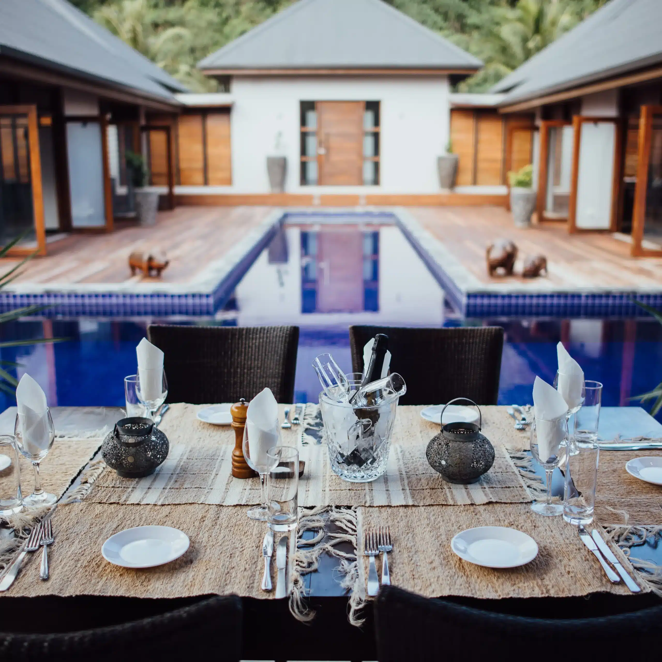 Set dining table with plates, glassware and folded napkins in the foreground, overlooking a blue courtyard swimming pool at a luxury retreat in Vanuatu.