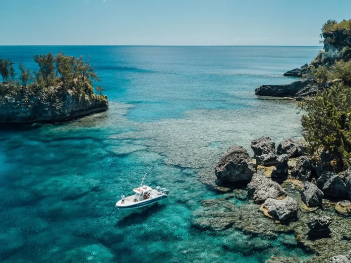 Boat anchored in crystal-clear turquoise water near a rocky tropical coastline and reef lagoon in Vanuatu under a blue sky.