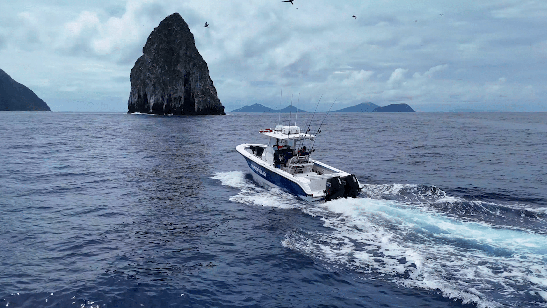 Ocean Blue Fishing Adventures fishing boat cruising on the open ocean near a volcanic sea stack in Vanuatu.