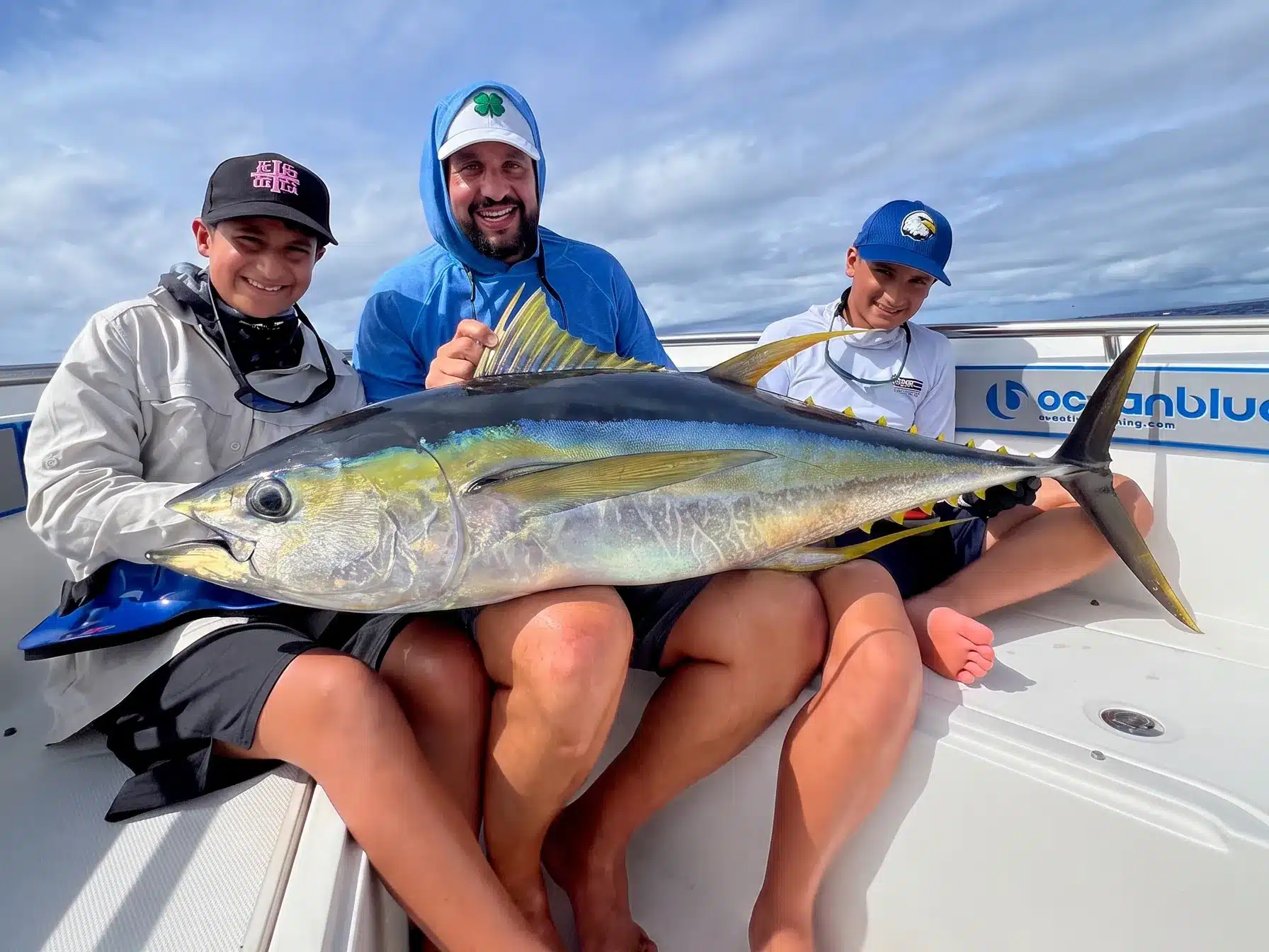 Three anglers holding a large yellowfin tuna on an Ocean Blue Fishing Adventures boat in Vanuatu, smiling after an offshore fishing trip.