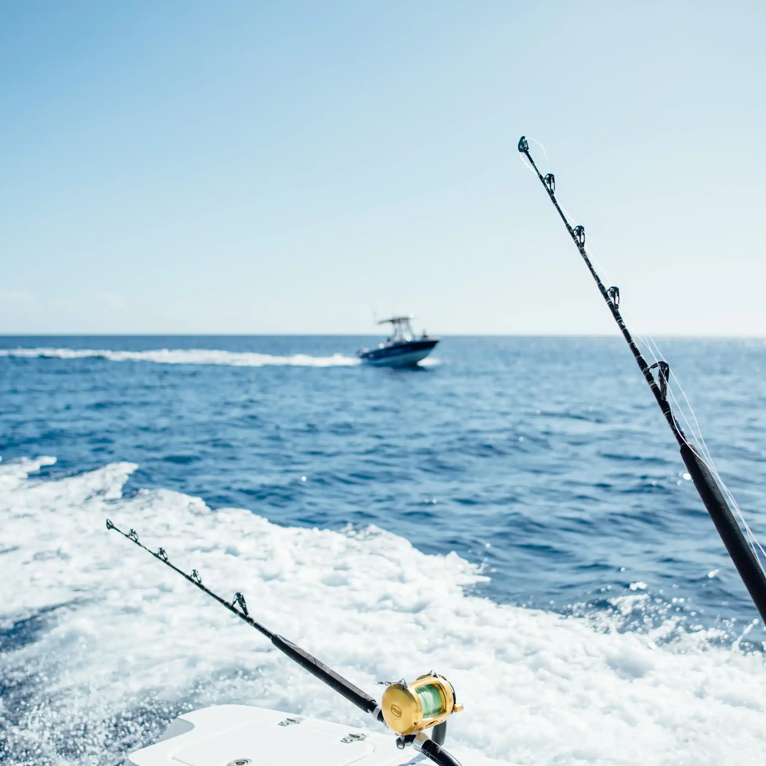 Fishing rods set up on a boat with another sport fishing boat cruising in the distance on open ocean, ready for a beginner fishing trip.