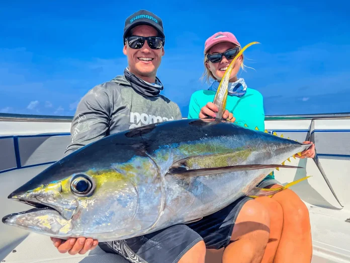 Two anglers holding a large yellowfin tuna on a sport fishing boat in Vanuatu under a clear blue sky.