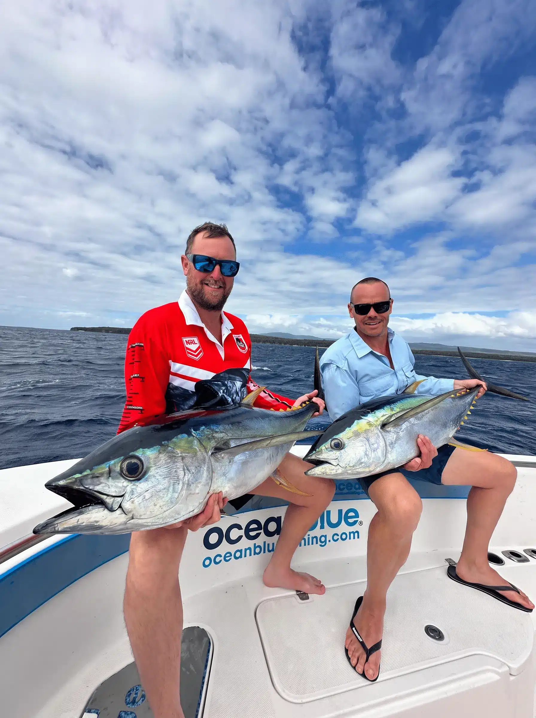 Two anglers holding yellowfin tuna on an Ocean Blue Fishing Adventures boat in Vanuatu, with open ocean and cloudy sky in the background.