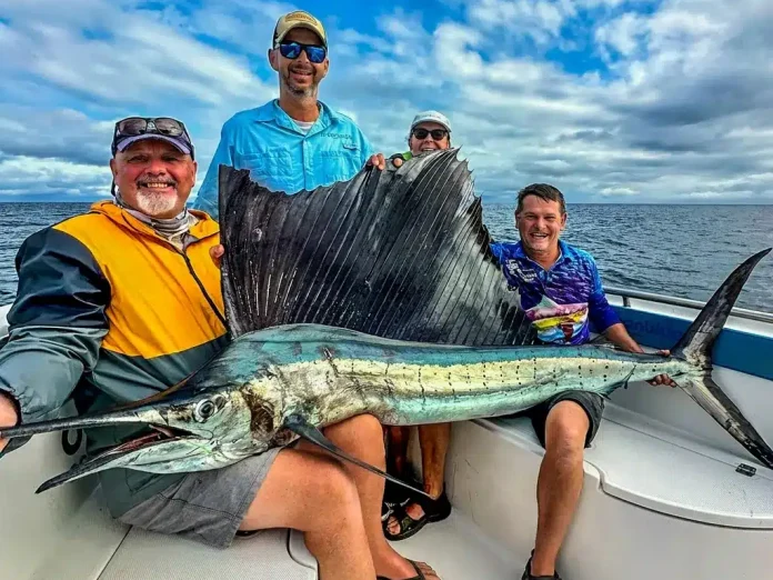 Group of anglers posing with a large sailfish on a sport fishing boat in Vanuatu, showing the raised sail and long bill on open water.