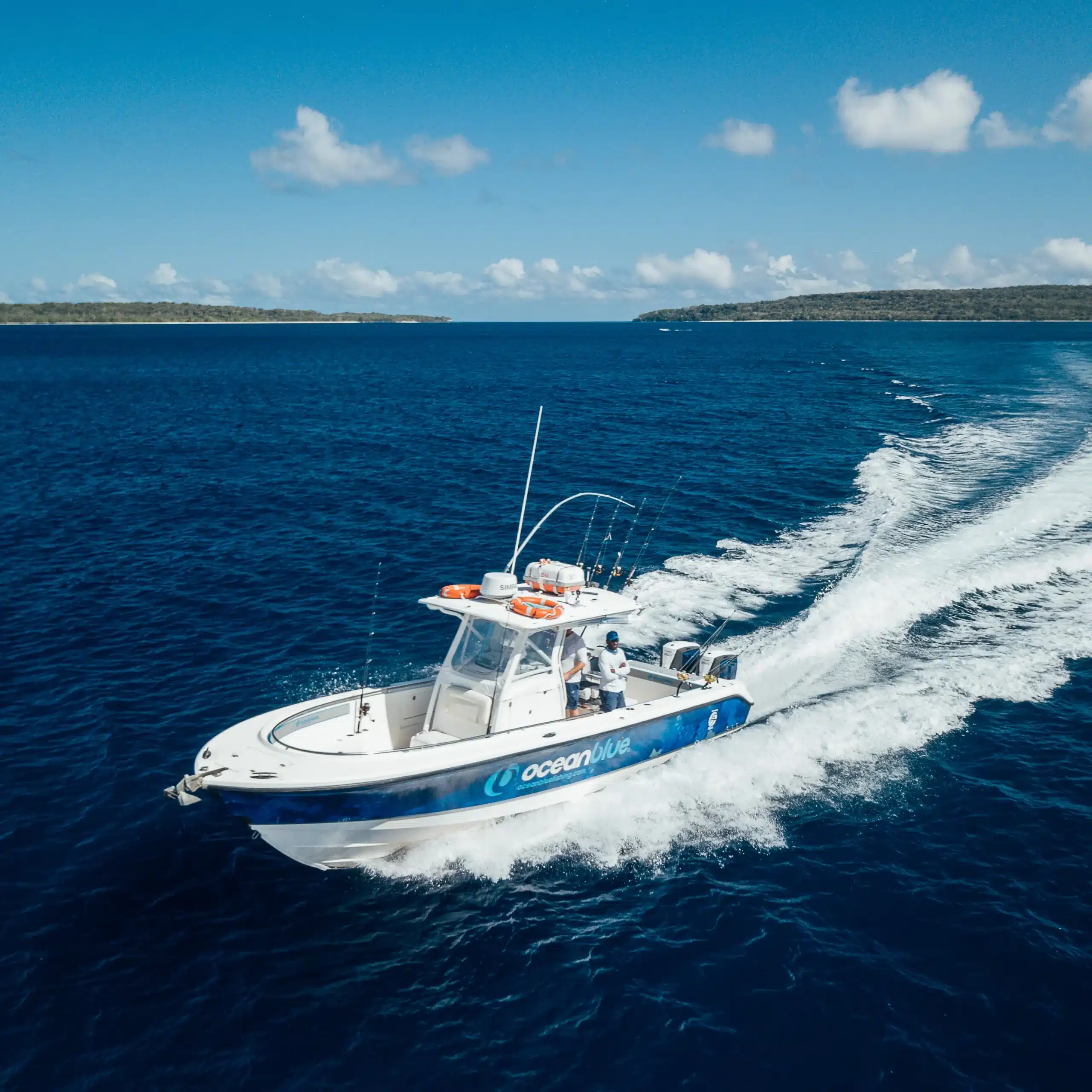 Ocean Blue Fishing Adventures centre-console sport fishing boat speeding across deep blue water in Vanuatu, leaving a white wake with island coastline in the distance.