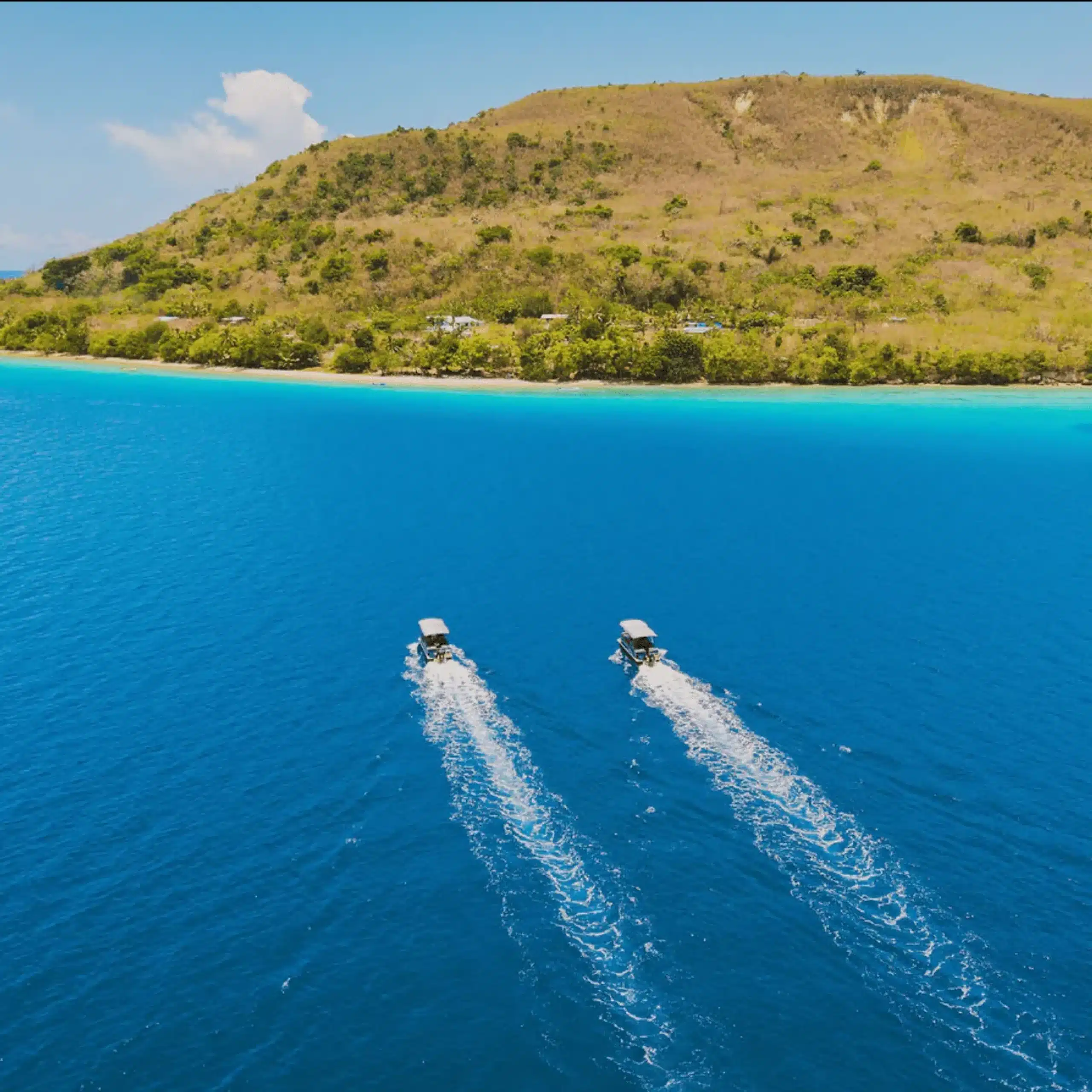 Aerial view of two boats cruising across bright blue water toward a tropical coastline in Vanuatu during a private snorkelling cruise.