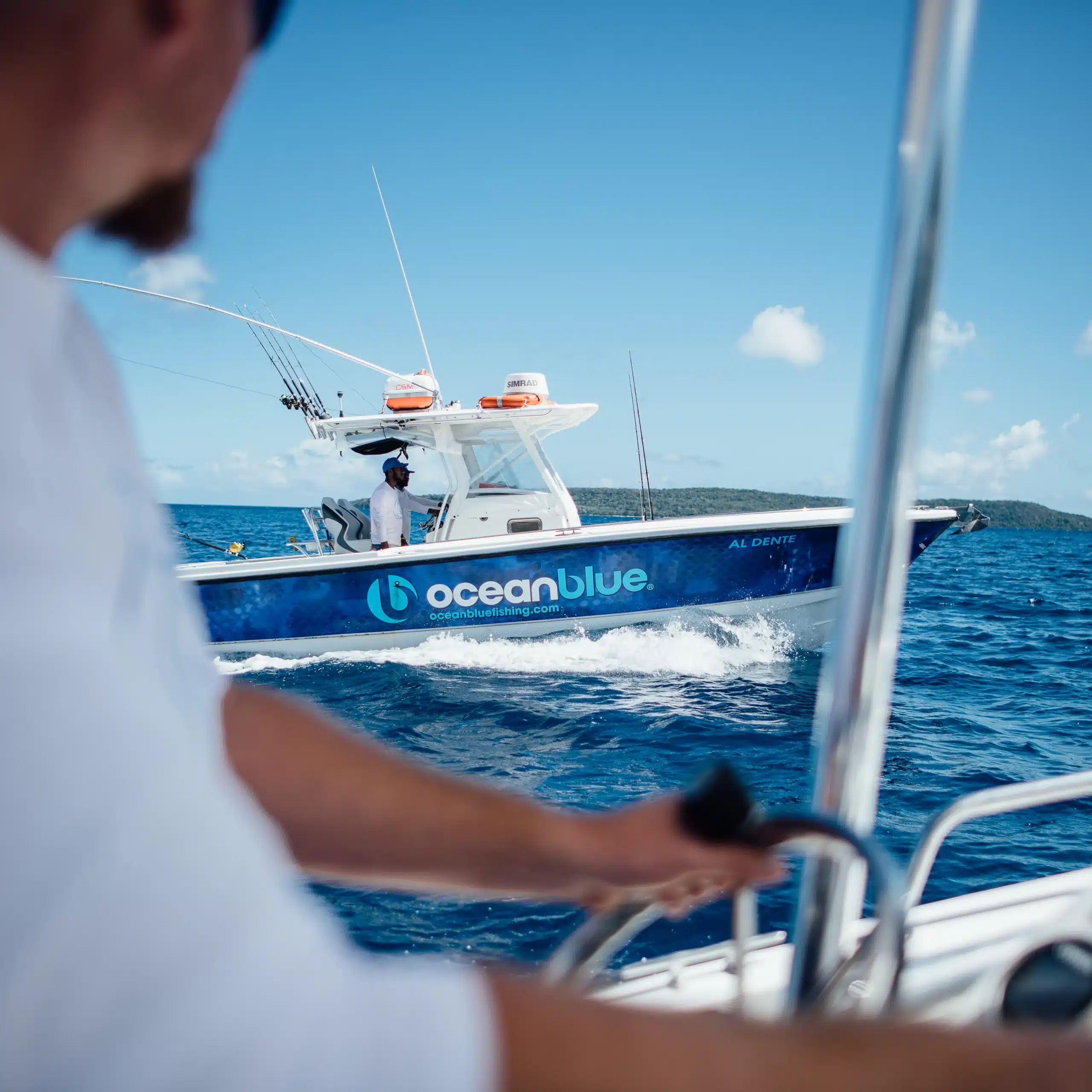 Ocean Blue Fishing Adventures centre-console boat cruising on blue water in Vanuatu, photographed from another boat with a skipper in the foreground.