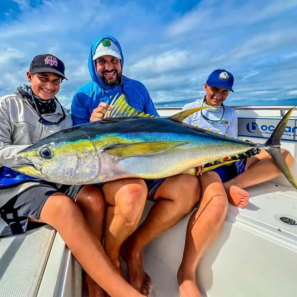 Three anglers holding a large yellowfin tuna on an Ocean Blue Fishing Adventures boat in Vanuatu, smiling after a successful offshore fishing session.