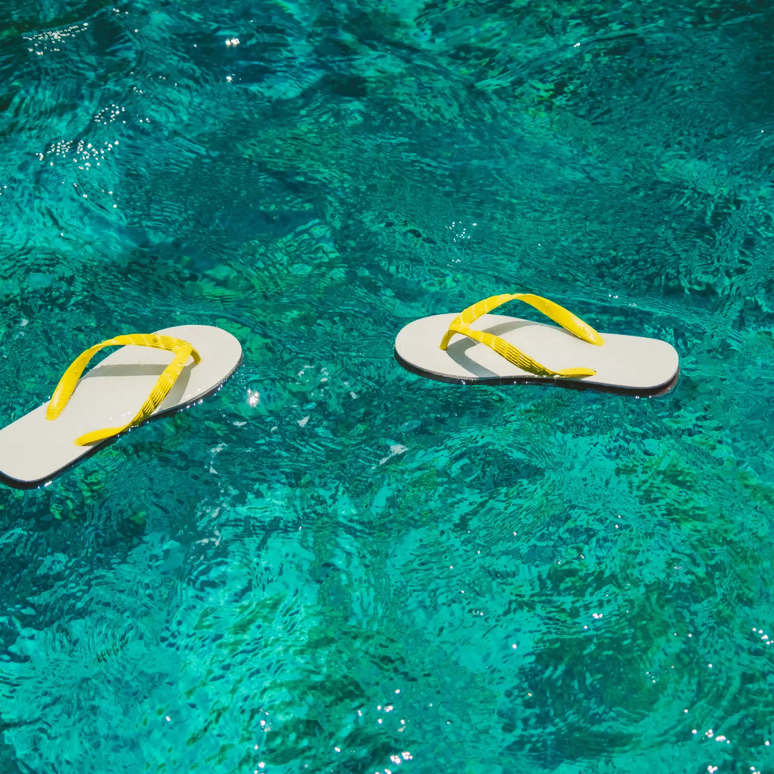 Two white flip-flops with yellow straps floating on clear turquoise water, illustrating a relaxed snorkelling cruise vibe in Vanuatu.
