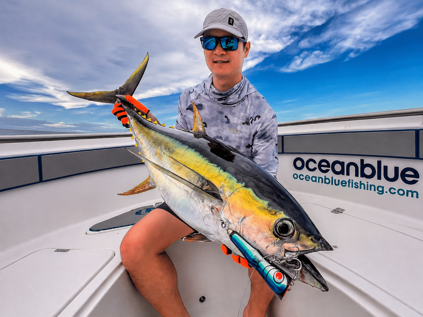 Angler holding a yellowfin tuna on an Ocean Blue Fishing Adventures boat in Vanuatu, with a trolling lure in the fish’s mouth and the Ocean Blue logo visible.