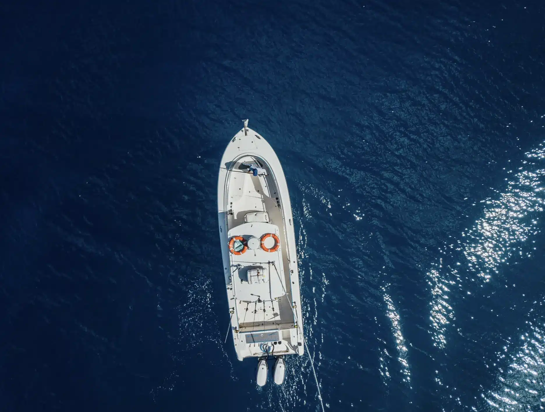 Aerial top-down view of a sport fishing boat on deep blue ocean water, showing an uncrowded, open-water fishing scene.