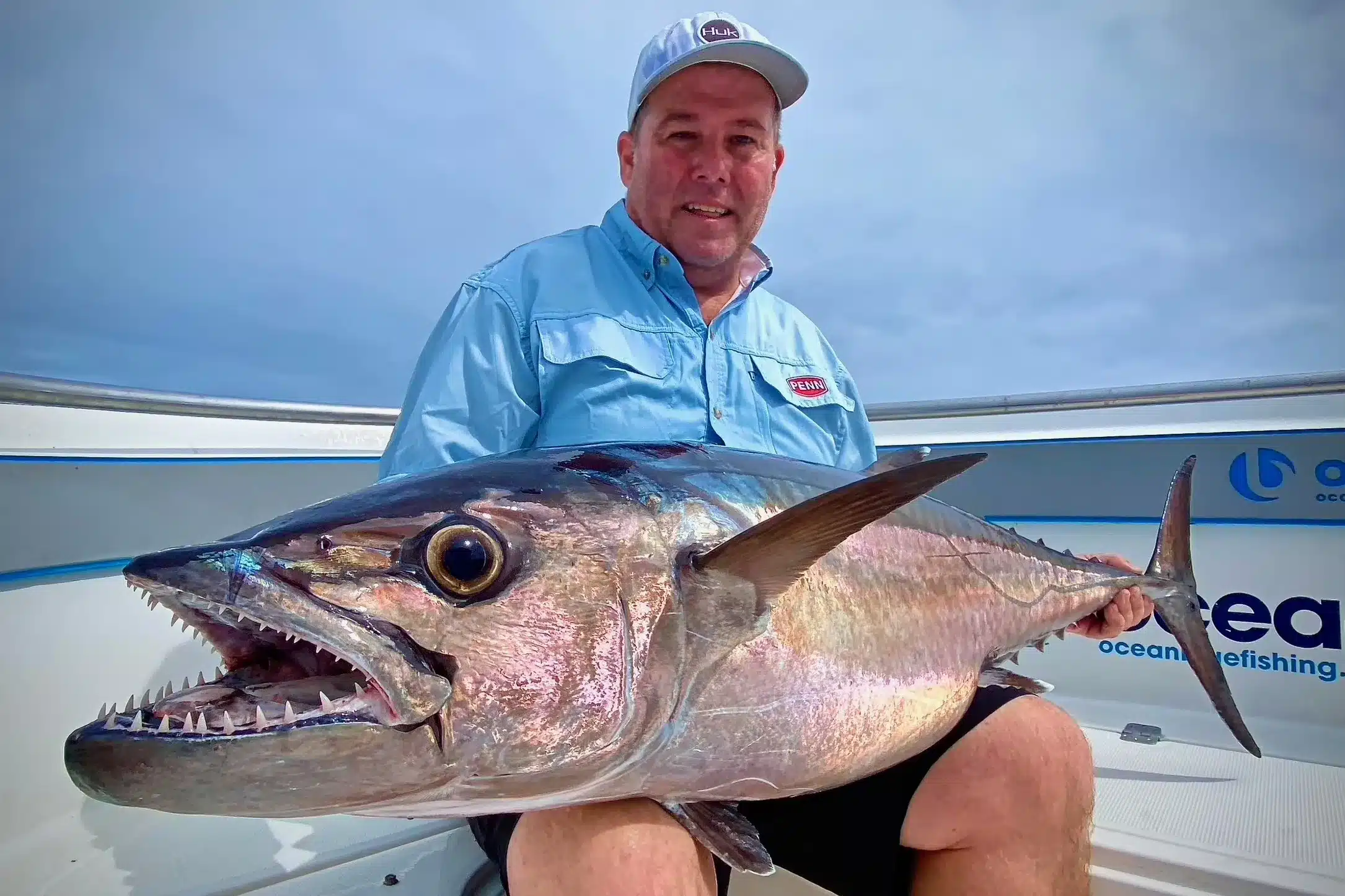 Angler holding a large dogtooth tuna on an Ocean Blue Fishing Adventures boat in Vanuatu, showing the fish’s powerful jaw and teeth.