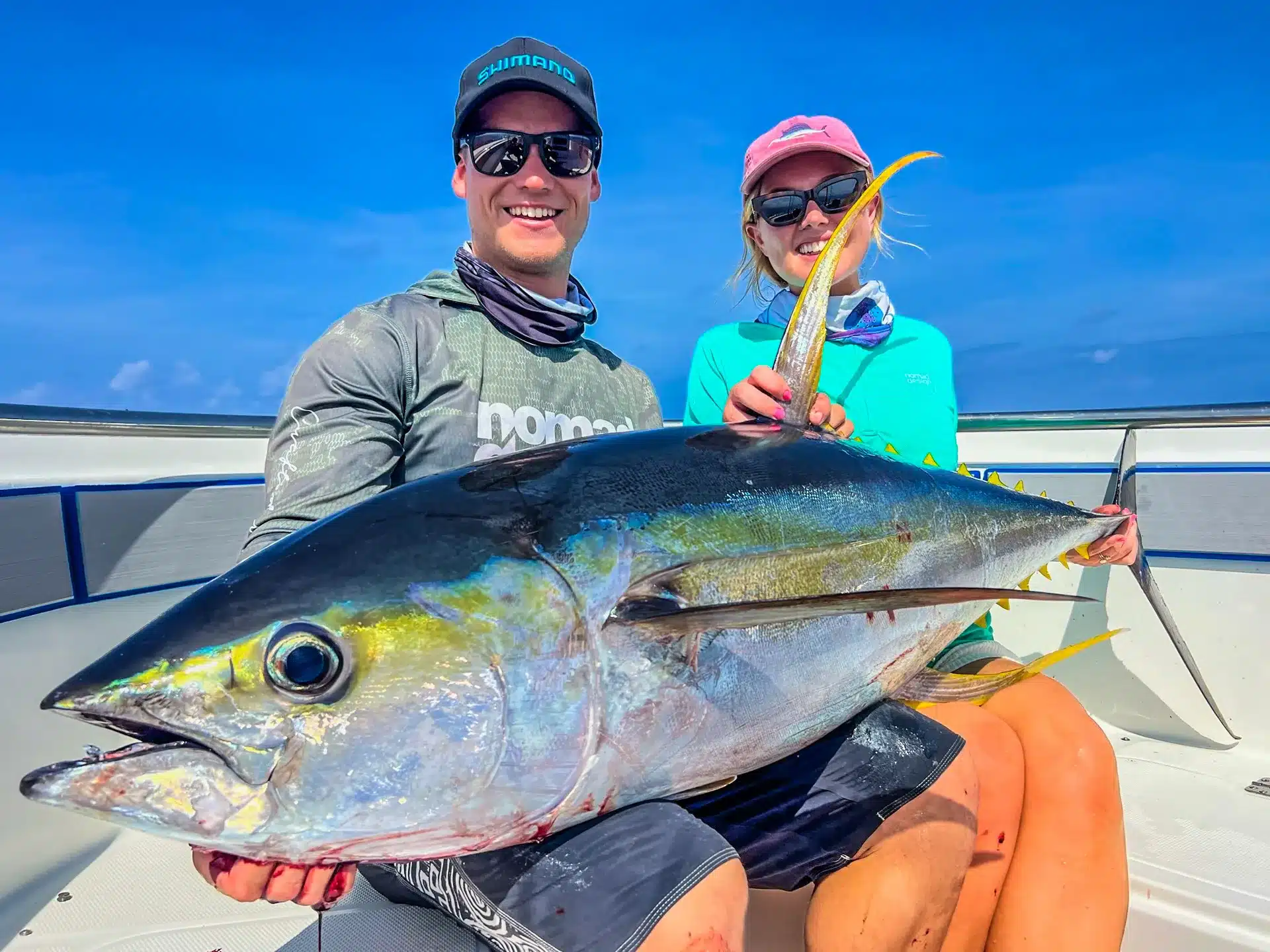 Couple holding a large yellowfin tuna on a sport fishing boat in Vanuatu under a clear blue sky, smiling after a successful offshore session.