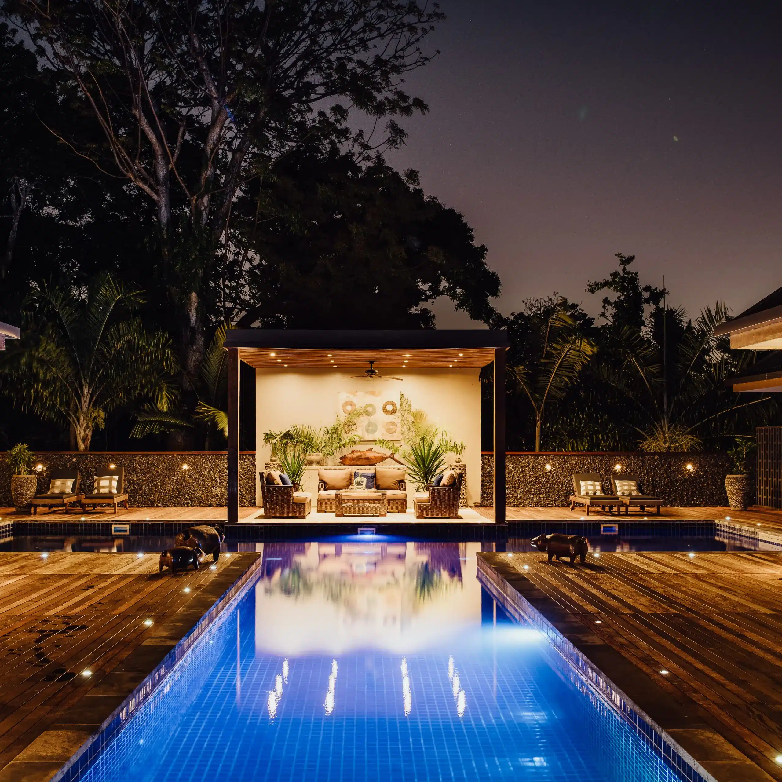Luxury resort pool at night with a lit cabana lounge area, timber deck and tropical gardens, creating a relaxing evening atmosphere in Vanuatu.