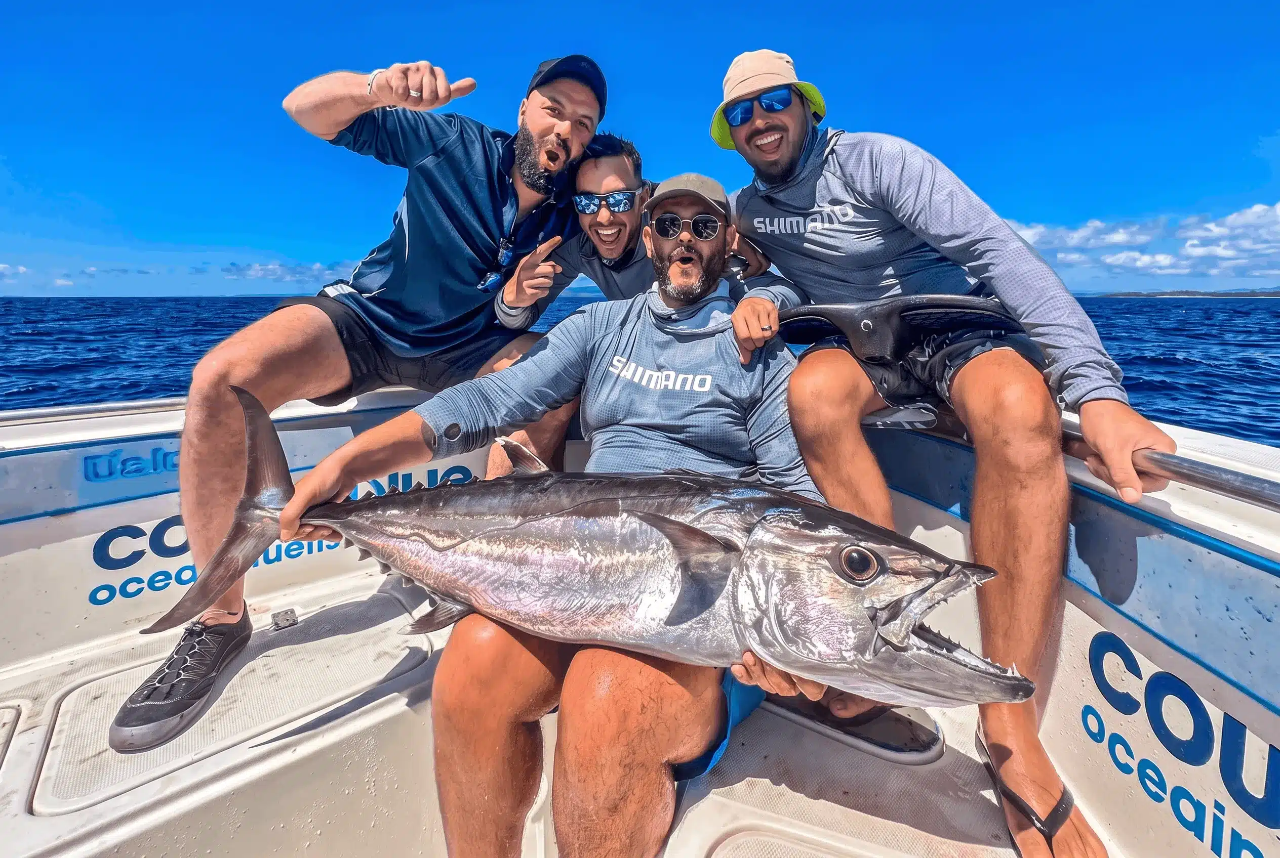 Group of friends posing with a dogtooth tuna on an Ocean Blue Fishing Adventures boat in Vanuatu, celebrating a successful fishing lodge trip.