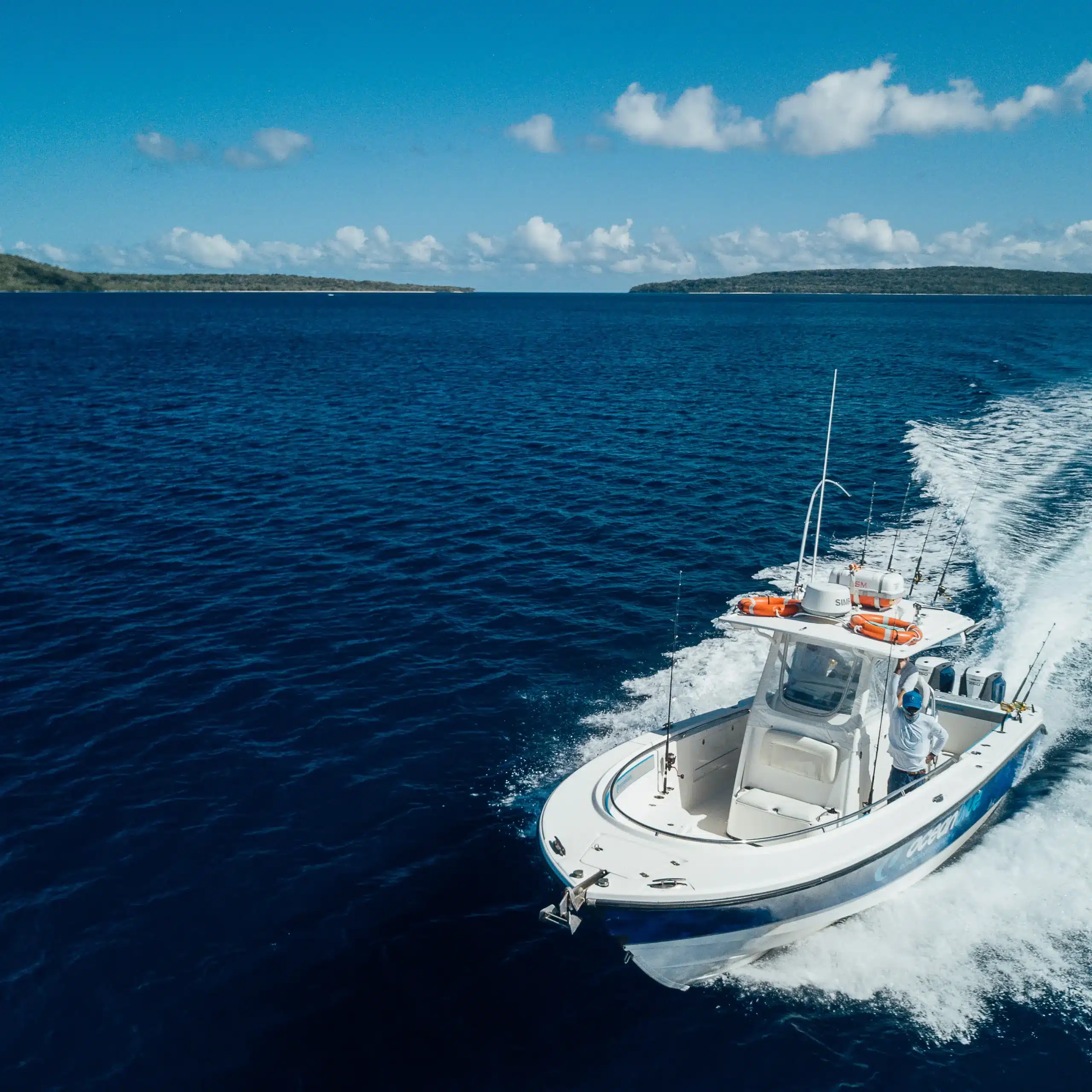 Ocean Blue Fishing Adventures centre-console boat running across deep blue water in Vanuatu, leaving a white wake with islands on the horizon.