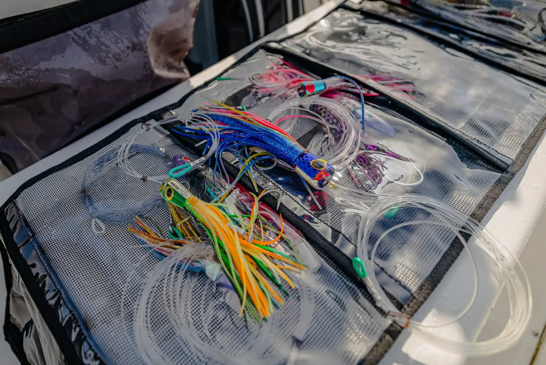 Close-up of a tackle roll with skirted trolling lures and leader lines laid out on a boat, prepared for marlin and tuna fishing.