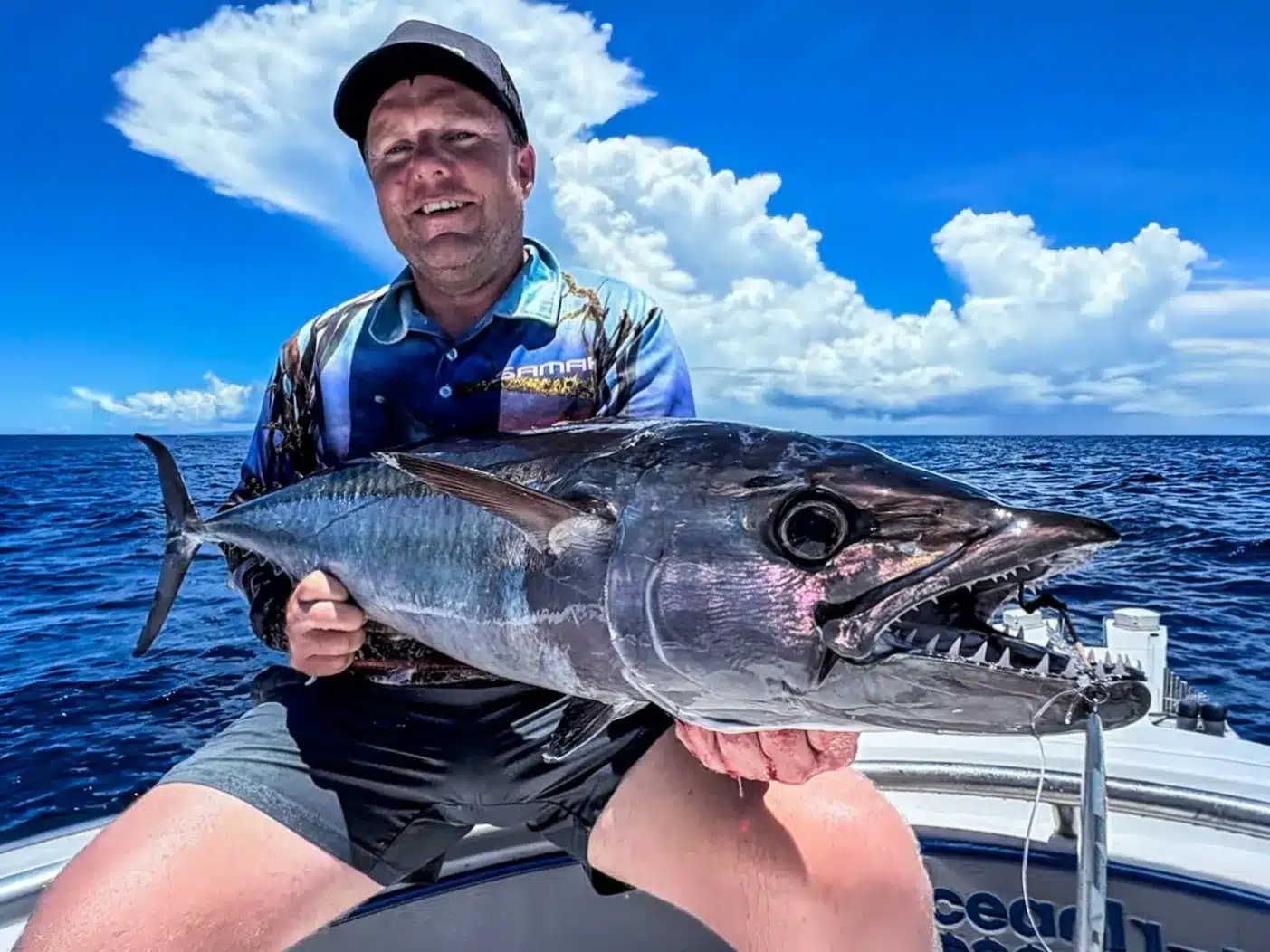 Angler holding a dogtooth tuna on a sport fishing boat in Vanuatu, with open ocean and dramatic clouds in the background.