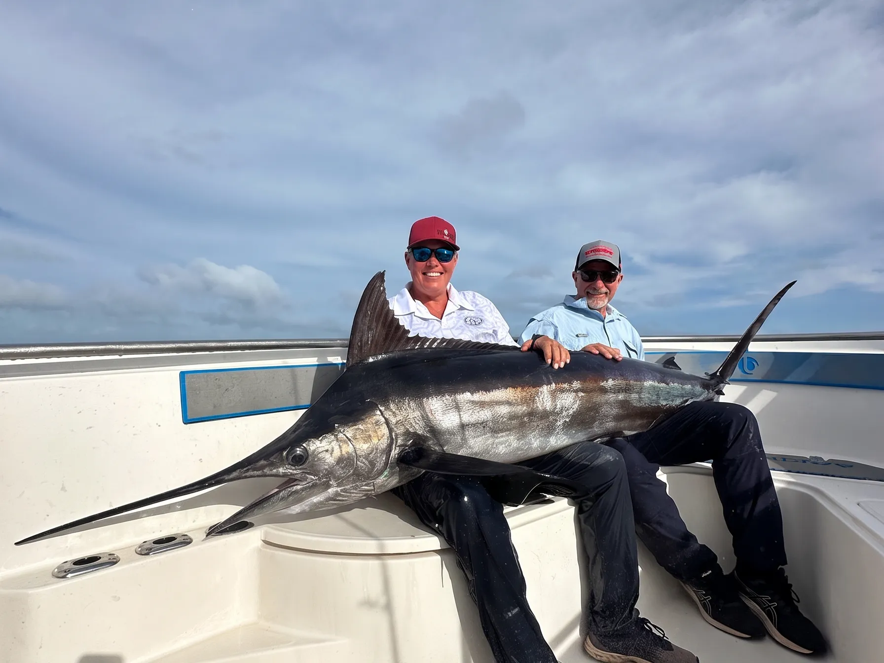 Two anglers posing with a large black marlin on a sport fishing boat in Vanuatu, with the marlin’s bill and dorsal fin visible.