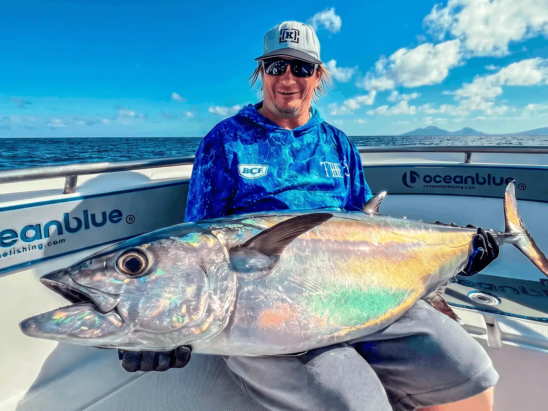 Trolling rod with a gold game reel and lure set out behind a boat on blue water in Vanuatu, with island coastline on the horizon.