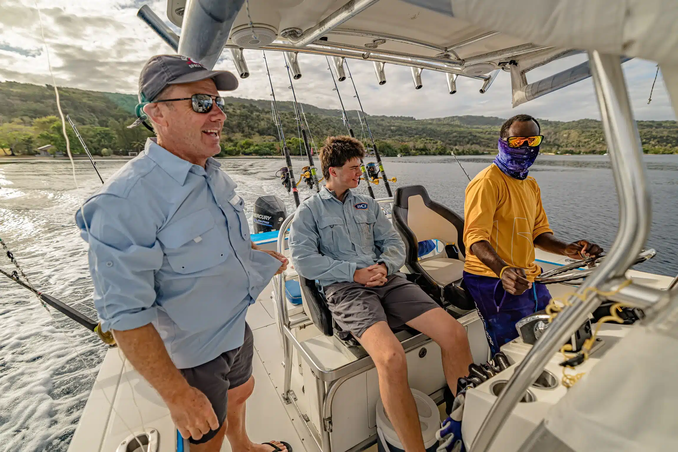 Guests and crew aboard an Ocean Blue Fishing Adventures boat in Vanuatu, cruising near the coastline with rods rigged for reef fishing.