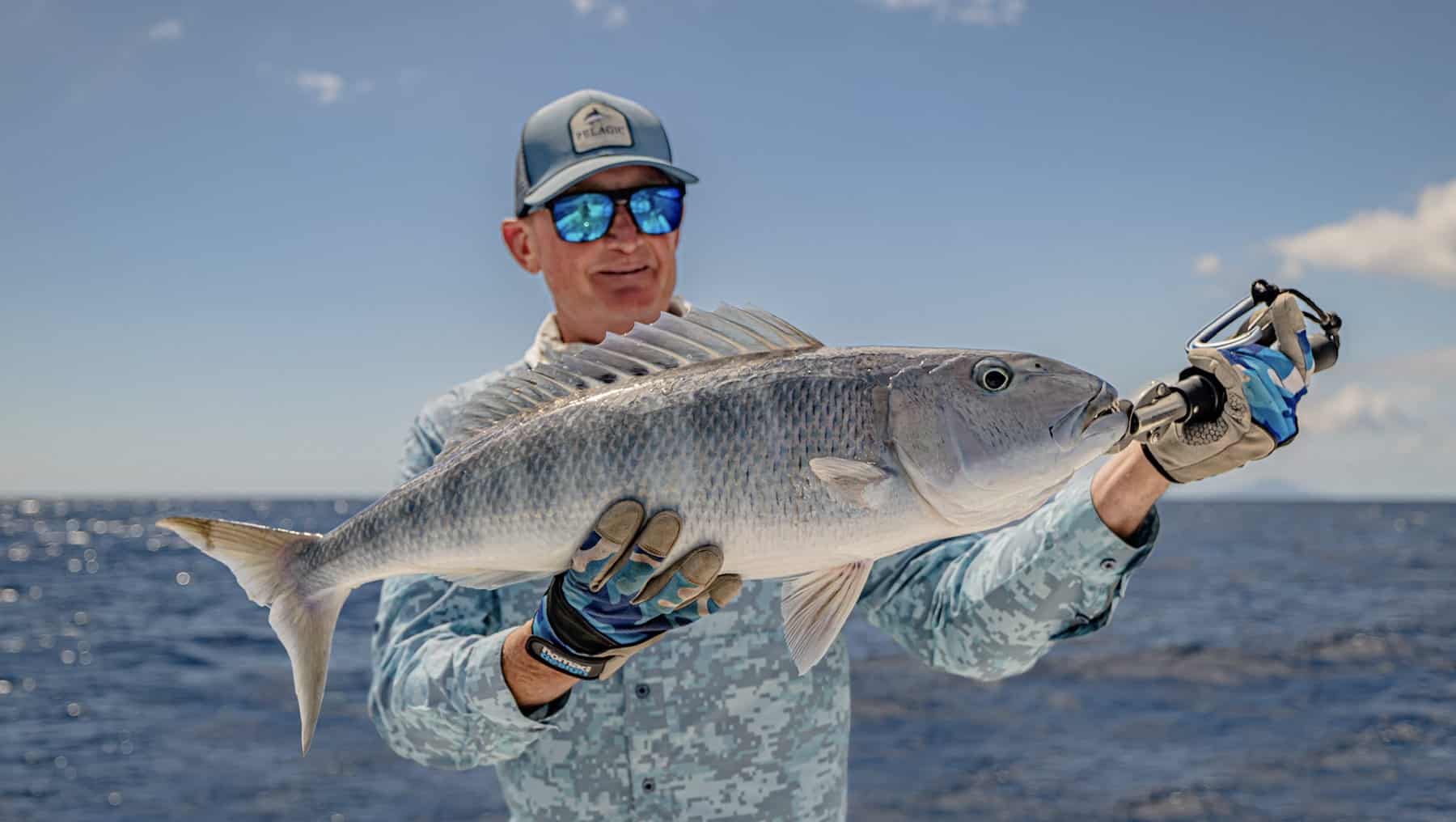 Angler holding a large jobfish caught while reef fishing in Vanuatu, with blue ocean in the background.